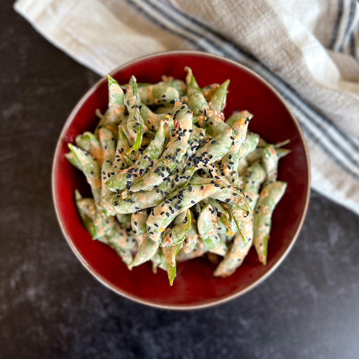Fiery edamame tossed in a creamy, spicy sauce and topped with black sesame seeds, served in a red bowl.