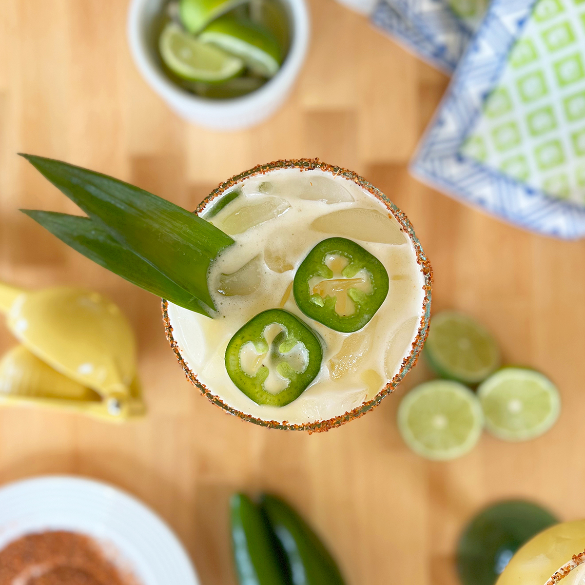 Pineapple jalapeño margaritas served over ice in glasses with Tajín-rimmed edges, fresh jalapeño slices, and pineapple leaf garnishes.